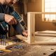 Professional using keyless chuck cordless drill assembling wooden furniture with various drill bits and accessories visible on workbench