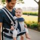 Parent smiling while carrying happy baby in ergonomic hip seat carrier during outdoor walk