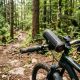 A waterproof Bluetooth speaker mounted on the handlebar of a mountain bike on a forest trail