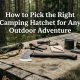 A camping hatchet rests on a wooden table surrounded by outdoor gear.