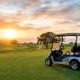 A modern electric golf cart parked on a green golf course fairway at sunset.
