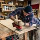 A person using a cordless jig saw to cut wood in a workshop.