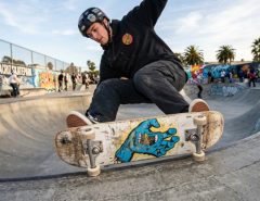 Skater landing a trick on a worn Santa Cruz deck at a California skatepark.