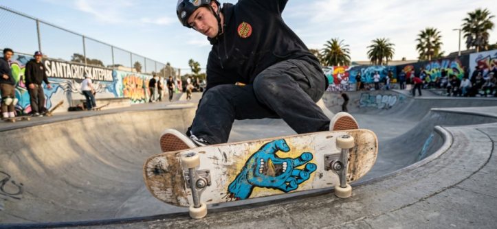 Skater landing a trick on a worn Santa Cruz deck at a California skatepark.