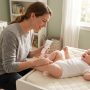 Parent gently applying moisturizing lotion to a baby's leg in sunlight.