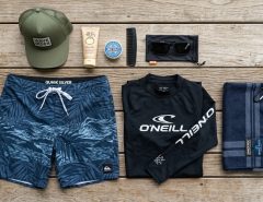 Flatlay of a practical surf clothing kit on a wooden deck.