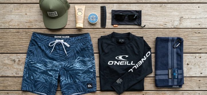 Flatlay of a practical surf clothing kit on a wooden deck.