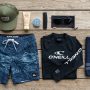 Flatlay of a practical surf clothing kit on a wooden deck.