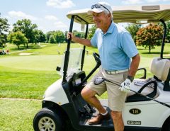 Older smiling male golfer driving an electric cart on a sunny fairway.