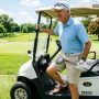Older smiling male golfer driving an electric cart on a sunny fairway.